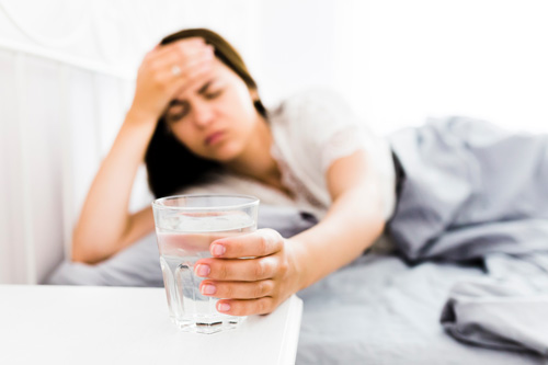 Migraines and Headaches - Women putting her hand on her head in bed grabbing a glass of water