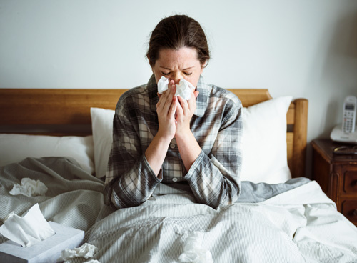 woman sitting in bed blowing her nose with the flu